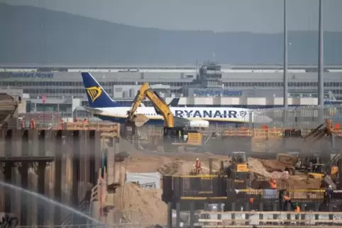 Ein Flugzeug rollt hinter der Baustelle zum neuen Terminal 3 am Flughafen vorbei. Der erste Flugsteig des neuen Terminals soll s