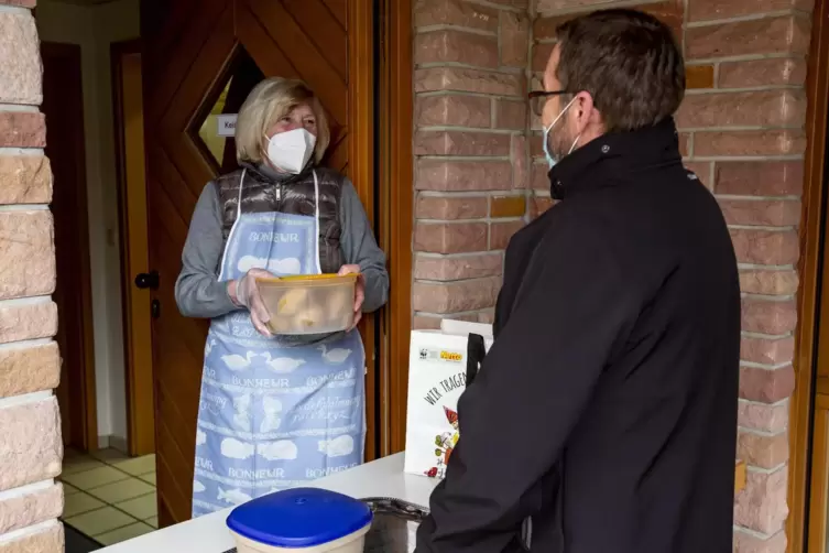 Die Corona-Regeln werden eingehalten: Ingrid Helf übergibt Thomas Kempf seinen Hering mit Kartoffeln. Das Essen stellt sie auf d