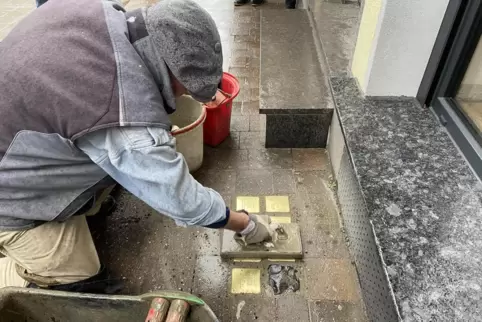 Trotz des Regens schlämmt Künstler Gunter Demnig Fugenmaterial zwischen die einzelnen Stolpersteine, damit diese fest im Bürgers