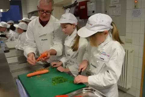 Küchenchef Thomas Langhauser zeigt den Miniköchen, wie man Karotten schält. 