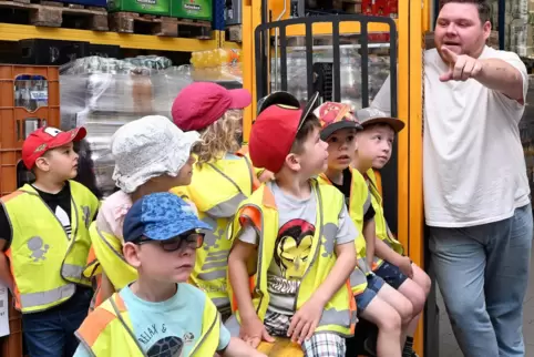 Edeka-Mitarbeiter Maximilian Bethge zeigt den Kindern, die auf einem Hubwagen sitzen, das Warenlager.