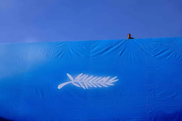 Ein Arbeiter hängt das offizielle Plakat der 77. Filmfestspiele von Cannes an der Fassade des Festival-Palais ’ auf. 