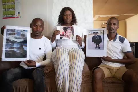 Trauernde Familie: Nomathamsanqa Vena (Mitte) und ihre beiden Brüder zeigen Fotos ihrer Tochter und Nichte Zenizole, die mit 15 