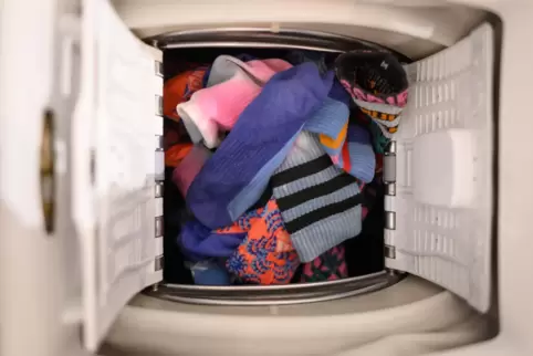  Bunte Socken liegen in der Trommel einer Waschmaschine. 