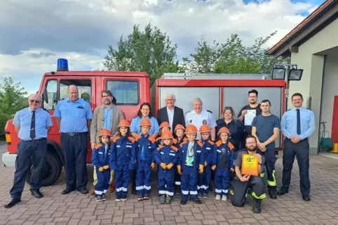 Professionell eingekleidet präsentieren sich neun von zehn Bambini-Feuerwehrleute mit Offiziellen und Gratulanten vorm Löschfahr