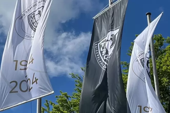 Vor der Sporthalle des TuS 04 Dansenberg künden drei neue Fahnen mit dem Logo und in den Vereinsfarben vom 100. Jubiläum der Spa