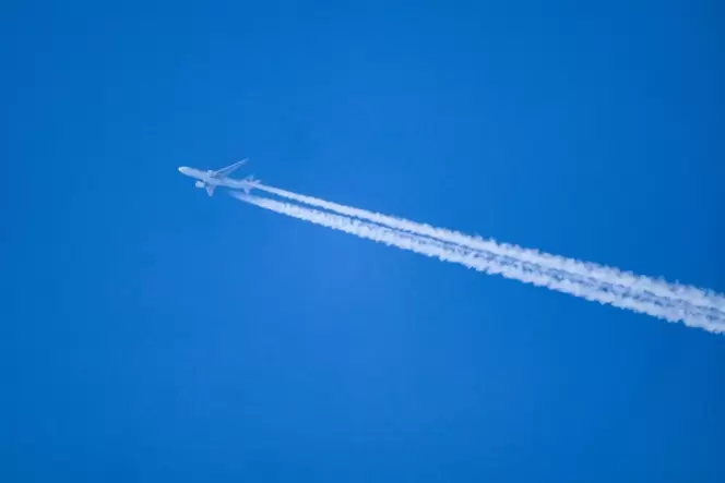 Ein Flugzeug hinterlässt Kondensstreifen am blauen Himmel.