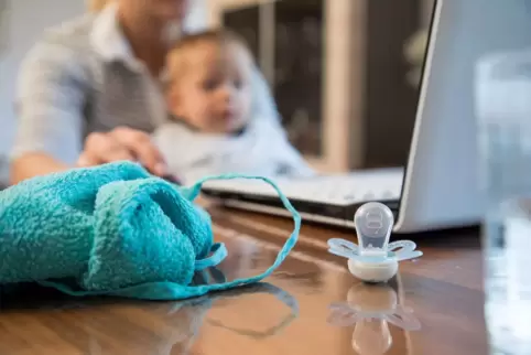 Eine Frau sitzt mit ihrem Sohn im Arm am Laptop