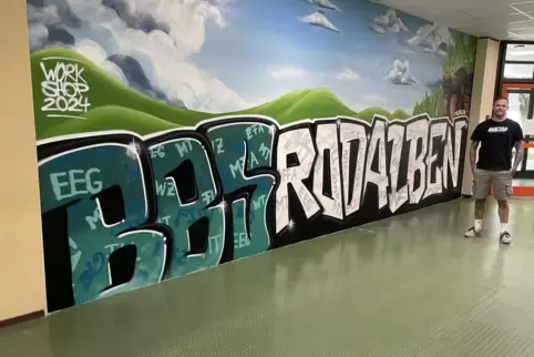 Der Graffiti-Schriftzug an einer Wand der Berufsbildenden Schule Rodalben. Künstler Daniel Ferino steht daneben. 