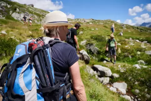 Eine Frau wandert mit Rucksack und Hut an einem Berg