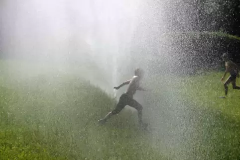 Mit einem Sprung durch eine Wasserwand kühlen sich diese Jungen ab. Kinder sind hitzeanfälliger als Erwachsene. 