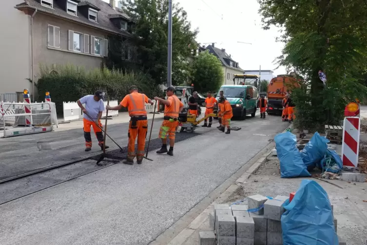 Zwischen den Straßenbahnschienen bringen die Arbeiter Asphalt ein. 