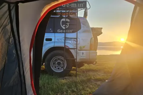 Der Blick aus dem Zelt fällt auf das Auto der Schorle Schrauwer und den Sonnenaufgang. Die Natur hat die Pfälzer unterwegs immer