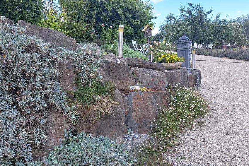 Von der Straße führt ein Weg hinab zum Hauseingang und zur Terrasse. Der steile Hang ist mit großen Findlingen gestützt. Die Ste