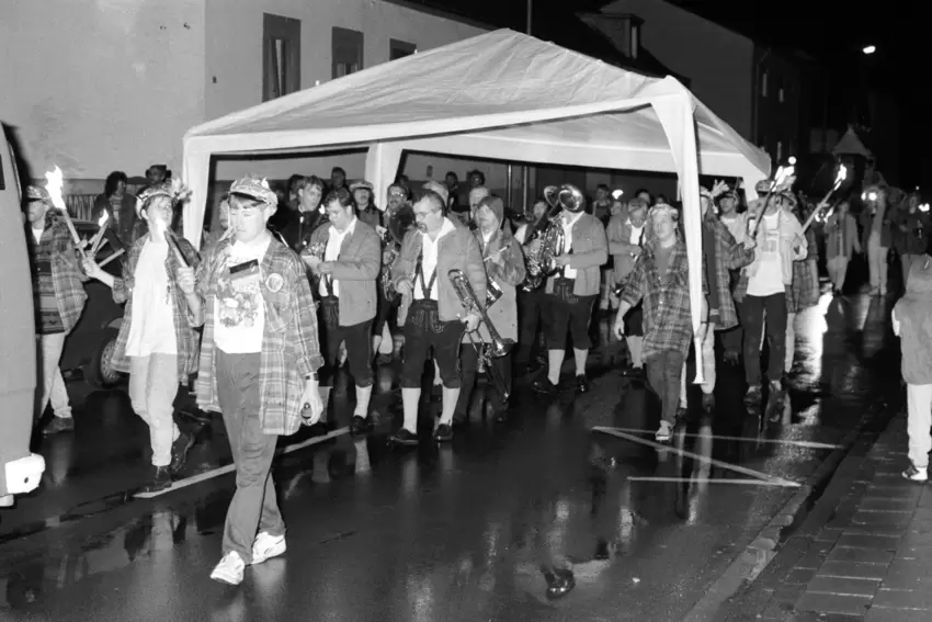 1994: Weil es beim Umzug regnet, wird die Musikkapelle kurzerhand mit einem tragbaren Pavillon geschützt.