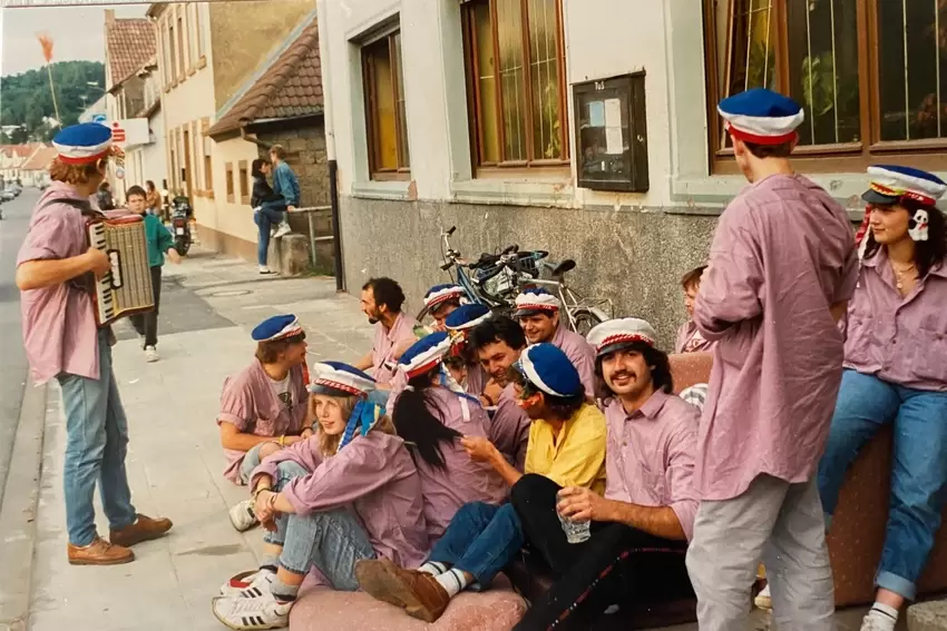 1990: Straßenszene mit den Straußbuben und Akkordeon- Live-Musik vor der früheren Wirtschaft »Zum Bahnhof« an der Ortsdurchfahrt