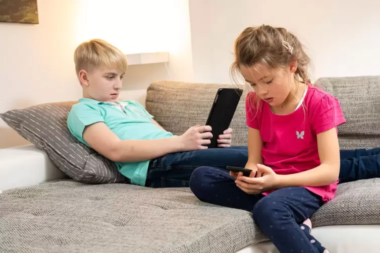 Zwei Kinder auf einer Couch spielen an Konsolen