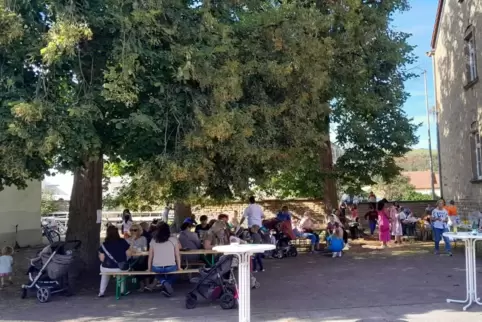 Kinder, Eltern und Besucher sitzen unter den Linden im Hof des Dorfgemeinschaftshauses Alsenz, in dem sich auch die Bücherei bef