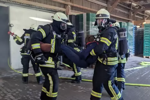 Unter Atemschutz retten die Feuerwehrmänner eine bewusstlose Person, die in einem verrauchten Gebäudeteil lag. 