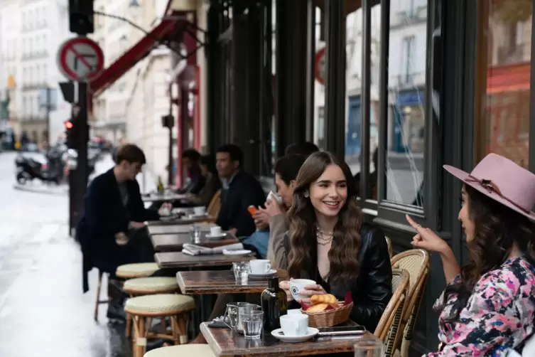 Emily (Lily Collins; Tochter von Phil Collins) in der Serie in einem Café in Paris.