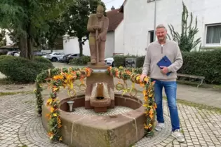 Der neue Maudacher Ortsvorsteher Andreas Olbert (CDU) am herbstlich geschmückten Torfstecherbrunnen.