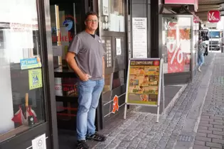 Arno Wagner mit seinem Klappschild vor der Apotheke. Im Hintergrund ist rechts ein Schaufenster des benachbarten Geschäfts zu se