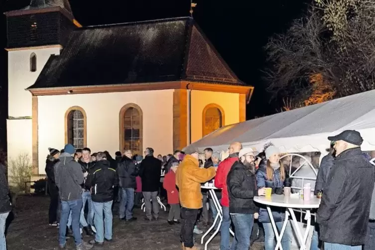 Bei einem Gläschen Glühwein und einer leckeren Wurst genießen viele Gäste das Miteinander vorm hell erleuchteten Gotteshaus.