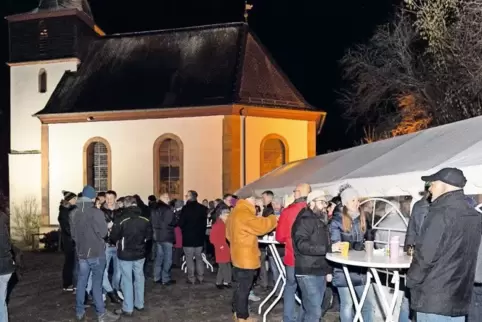 Bei einem Gläschen Glühwein und einer leckeren Wurst genießen viele Gäste das Miteinander vorm hell erleuchteten Gotteshaus.