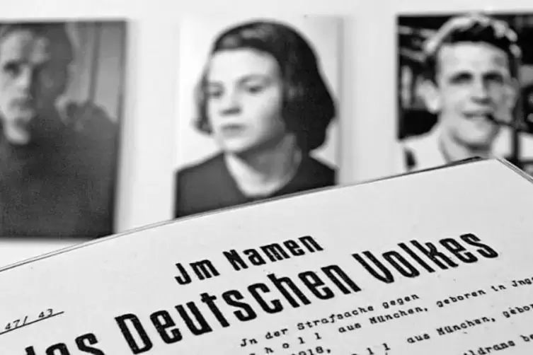 Eine Seite aus einer Gerichtsakte vor Fotografien der Weiße-Rose-Mitglieder Hans Scholl, Sophie Scholl und Christoph Probst (von