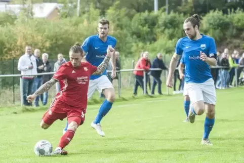 Mit Samuraifrisur am Ball: Patrick Freyer vom FC Queidersbach. Robin Cronauer und (rechts) Jacob William Weiler (FV Bruchmühlbac