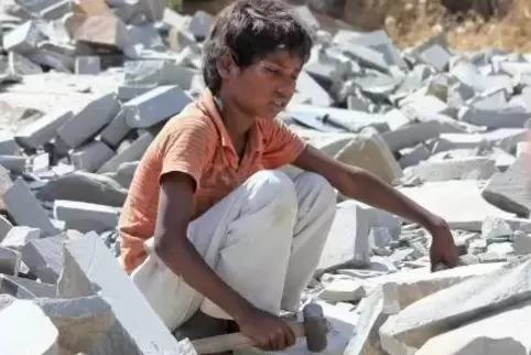 Ein kleiner Junge sitzt in der indischen Provinz Rajasthan mit einem Hammer auf Marmorsteinen. Tausende Kinder hauen in indische